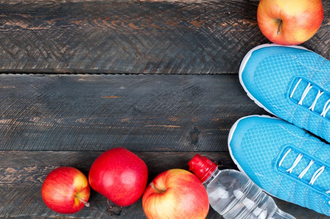 Sport concept. Sport shoes, apples and bottle of water on old wooden background. Sport equipment